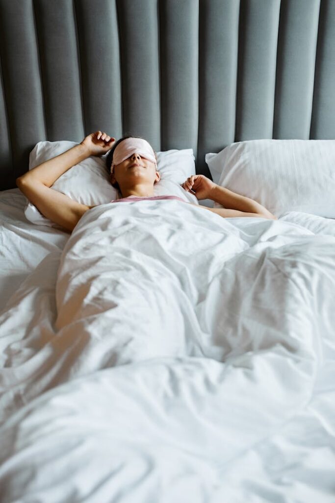 Relaxed woman wearing eye mask, comfortably sleeping in a cozy white bed.
